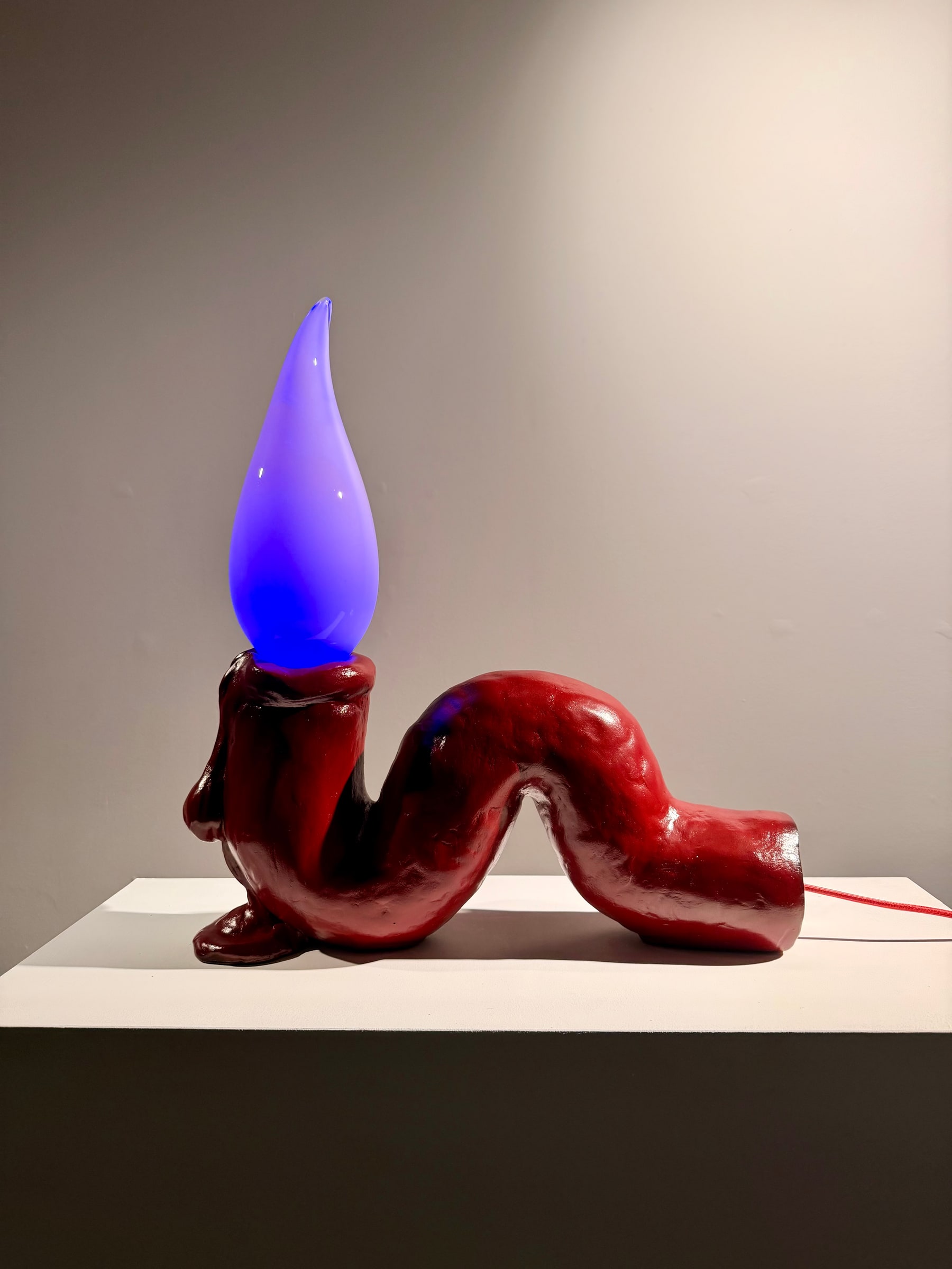 Tai Shani, Haunted by a Million Small Suns (Cardinal) (2025). Installation view of the lamp illuminated blue and violet on a wall-mounted shelf.