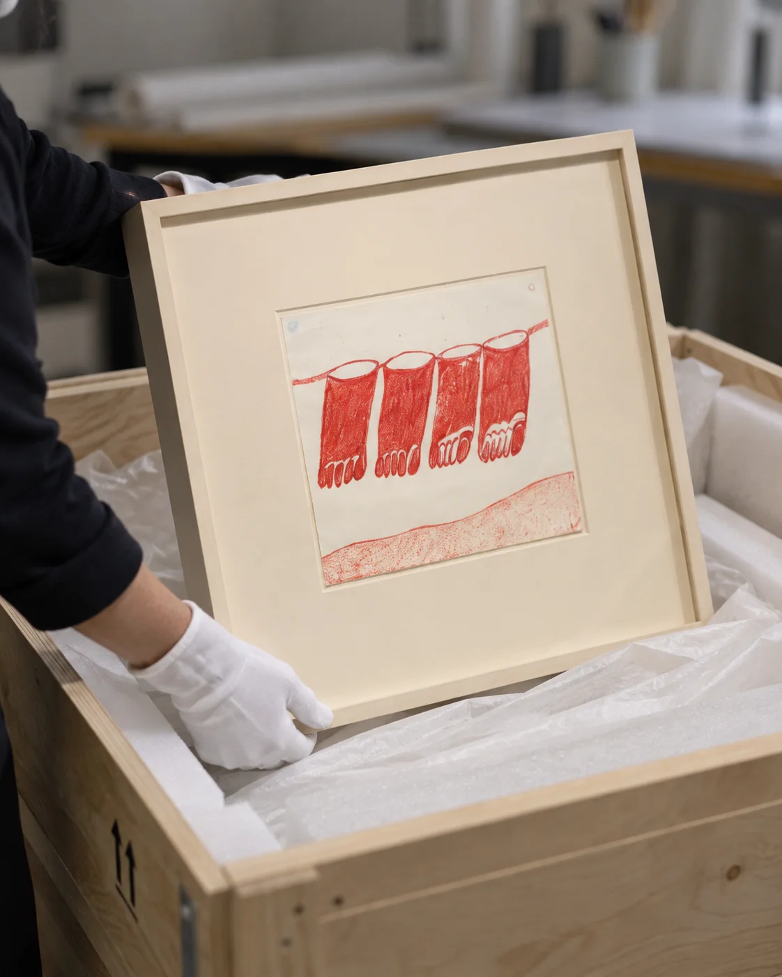 Gloved hands lifting a framed work on paper from a padded wooden art crate